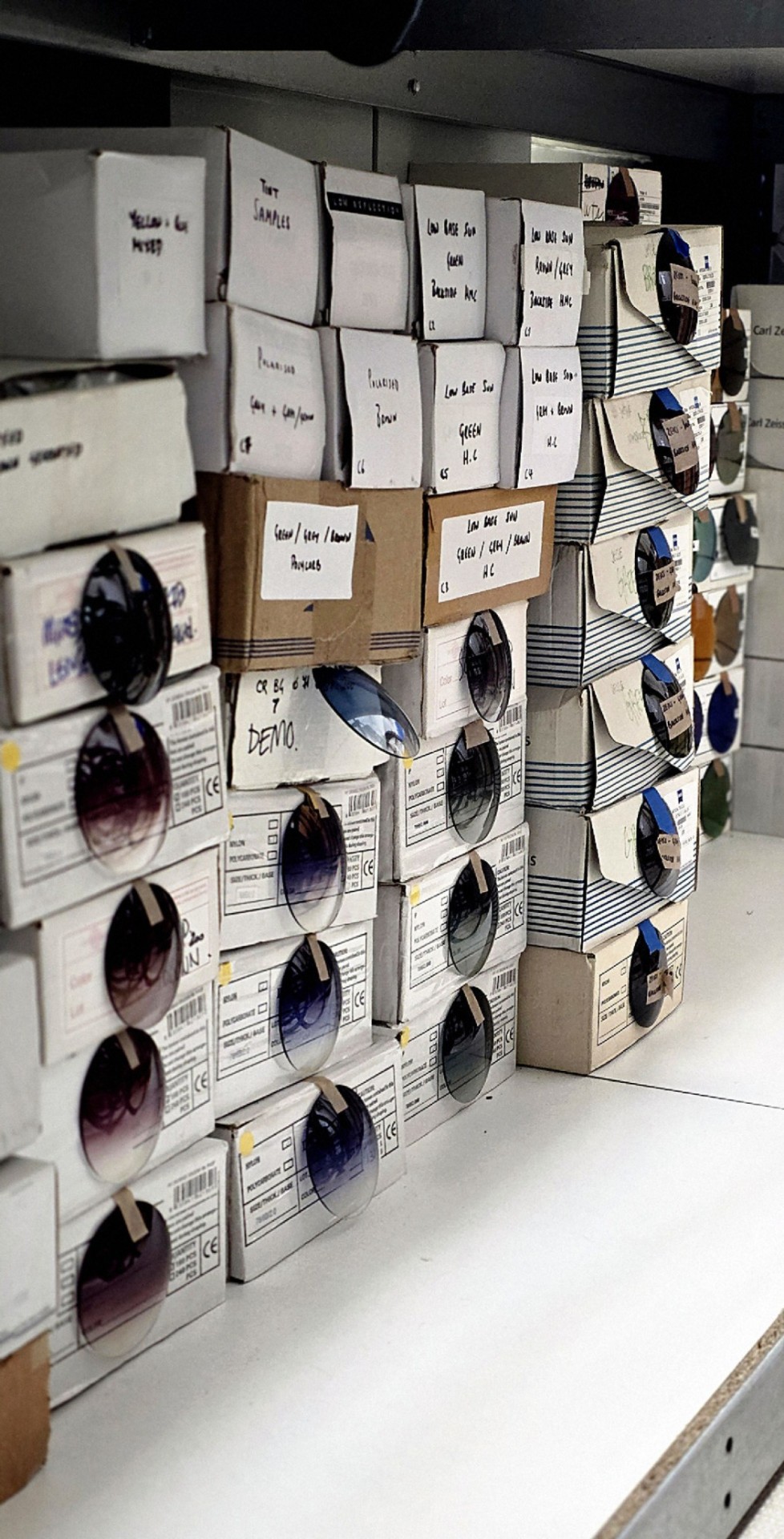 Hand-labelled lens stock boxes on the shelves of the East London lab